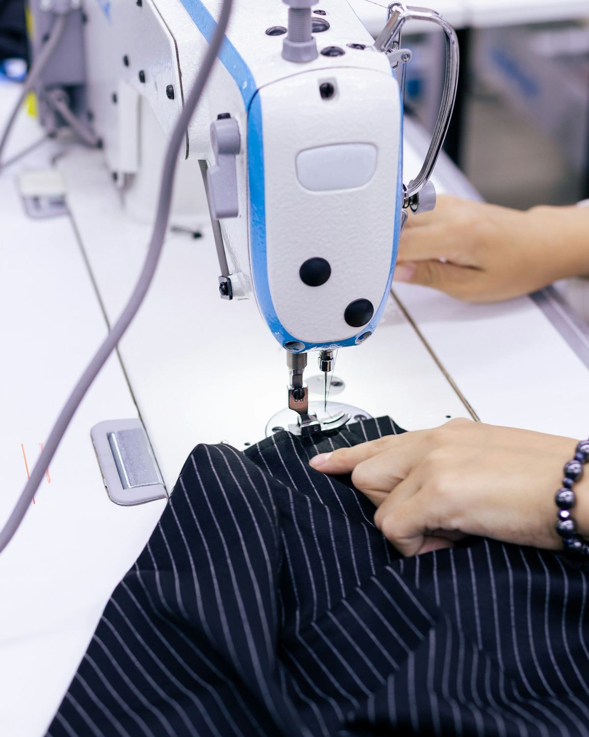Hands guiding striped fabric through an industrial sewing machine